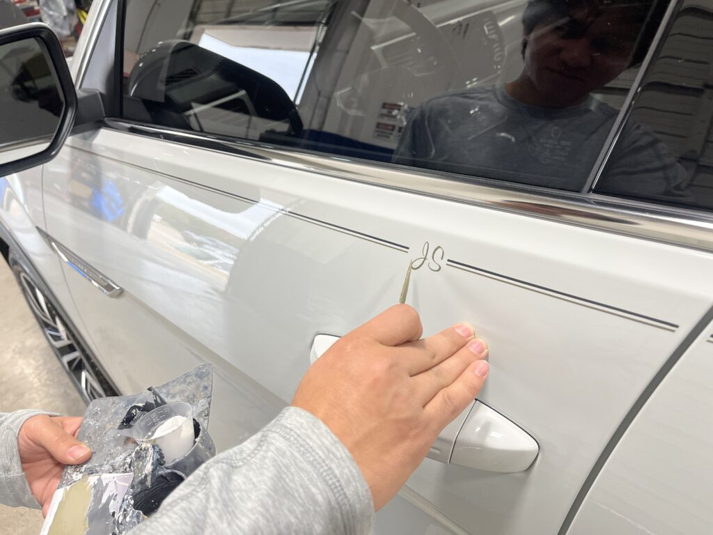 White VW Atlas pictured with custom hand painted pinstripes as the striper is adding a custom hand painted monogram logo with the customers initials artwork by Classic Pinstriping in the Dallas Fort Worth Metroplex