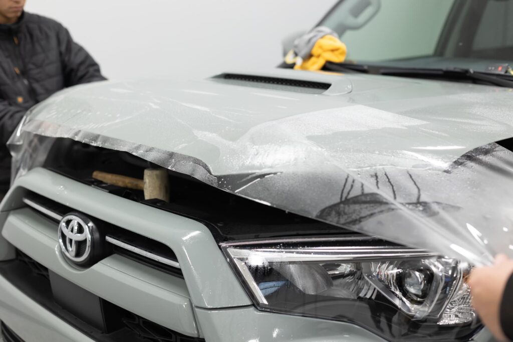 Installation of paint protection hood bra in process on gray Toyota SUV by Classic Pinstriping in Plano Texas